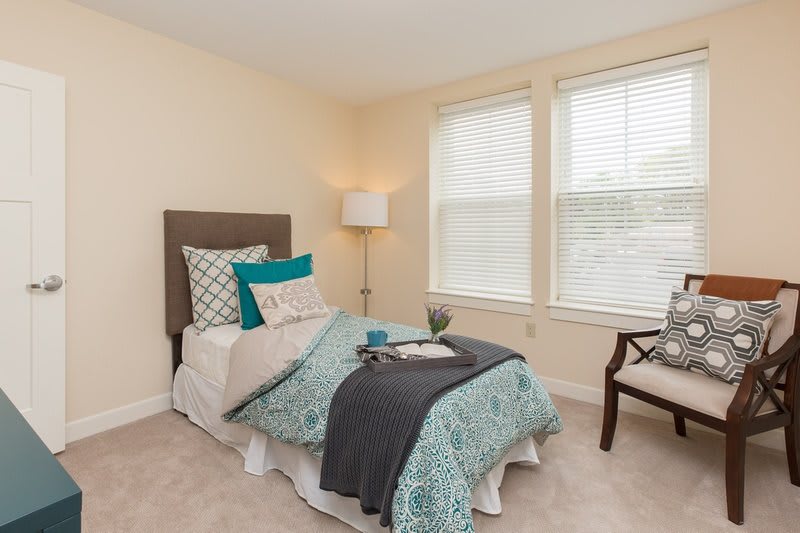 A cozy bedroom with a single bed, decorative pillows, and a floor lamp by the window.