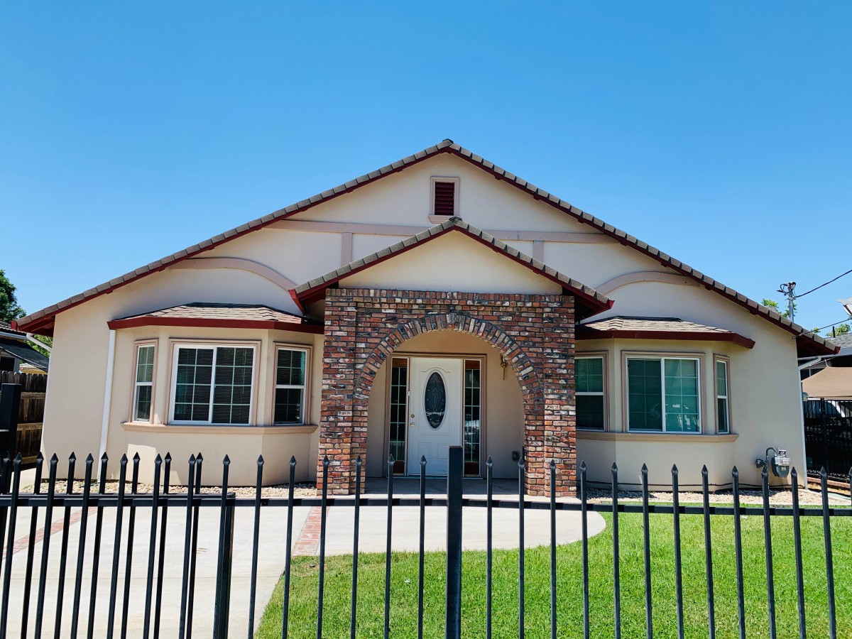 A residential house with a brick entrance and fenced front yard under a clear blue sky.