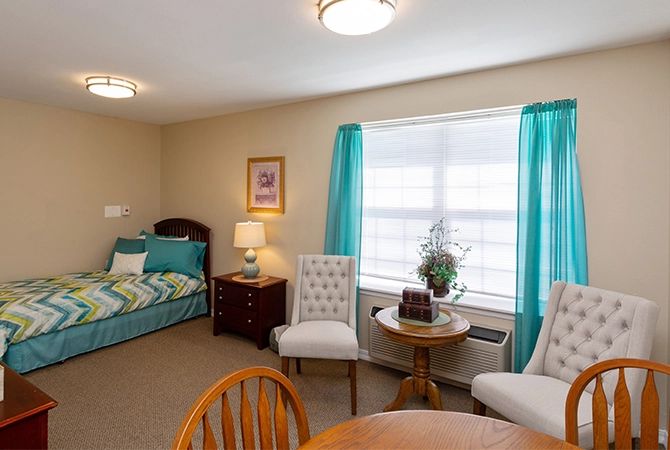 A cozy bedroom with a bed, chairs, and a window with blue curtains.