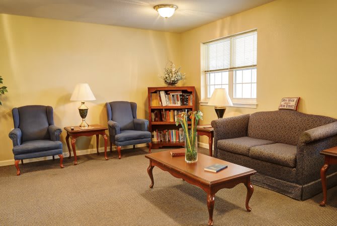 A cozy living room with a sofa, two armchairs, a wooden coffee table, and a bookshelf.