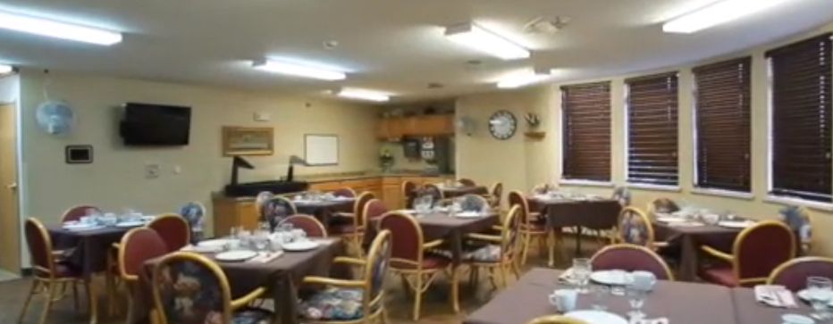 A cozy dining room with neatly arranged tables and chairs, featuring a small kitchen area in the background.