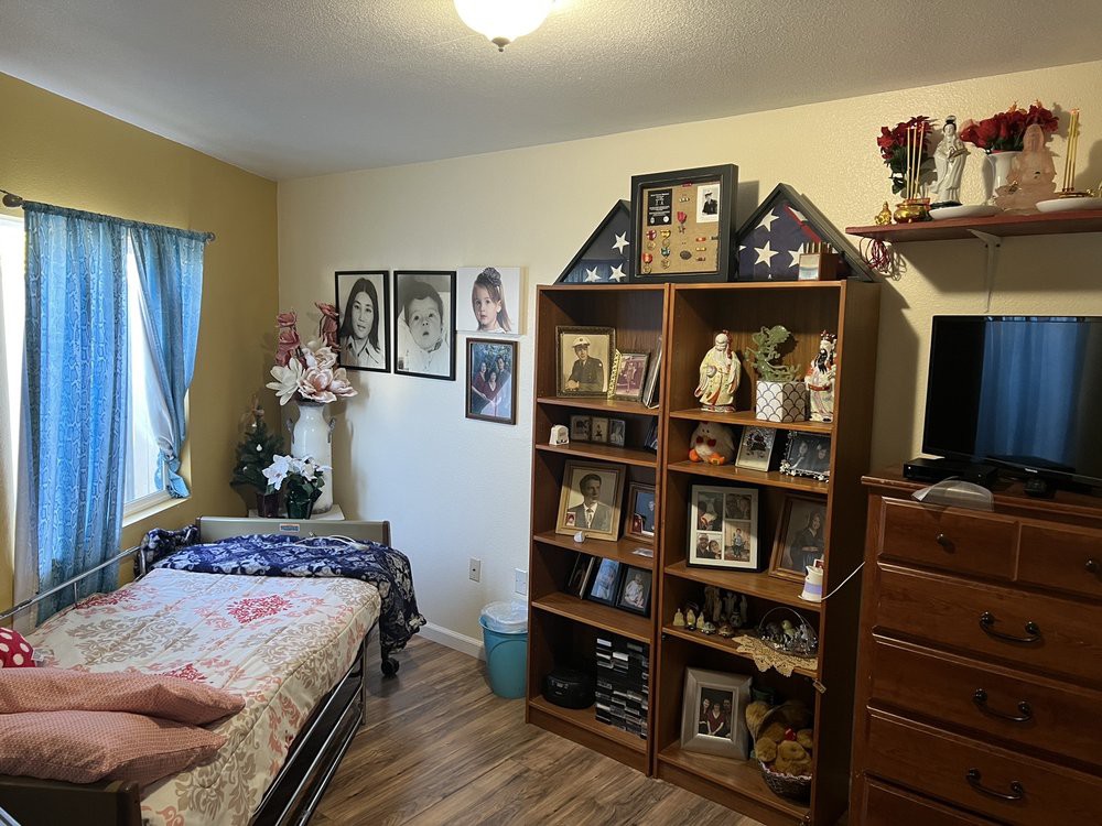 A cozy bedroom featuring a bed, decorated shelves with photographs and ornaments, and wooden furniture.