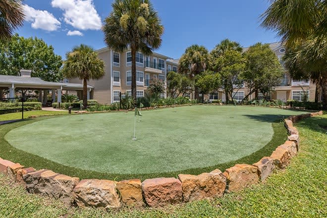 A scenic view of a putting green surrounded by palm trees and modern residential buildings.