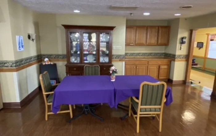 A dining area with a purple tablecloth-covered table and chairs set against a cabinet backdrop.