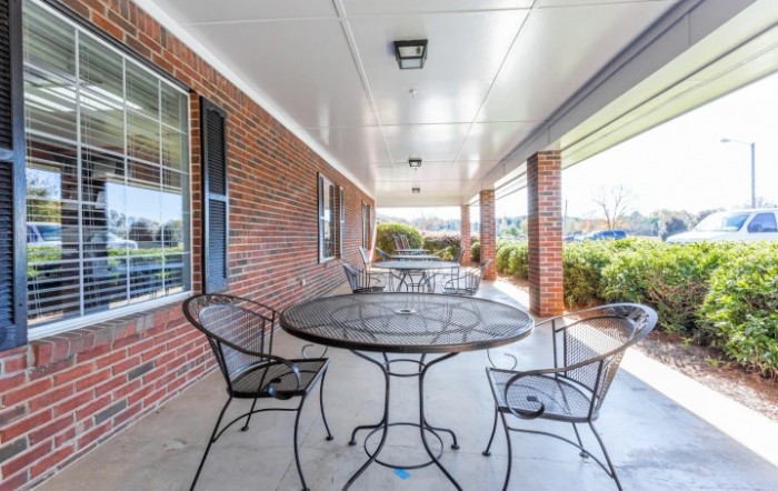 A cozy covered patio with iron table and chairs set against a brick wall.