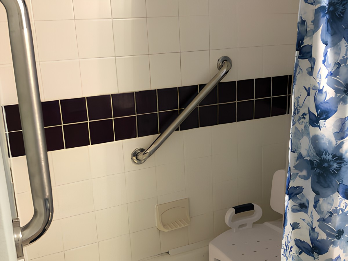 A bathroom with a grab bar installed on tiled walls for safety.