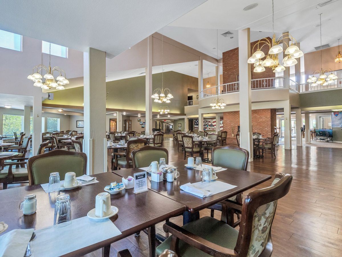 A spacious and elegantly decorated dining area with neatly arranged tables and chairs, illuminated by chandeliers.