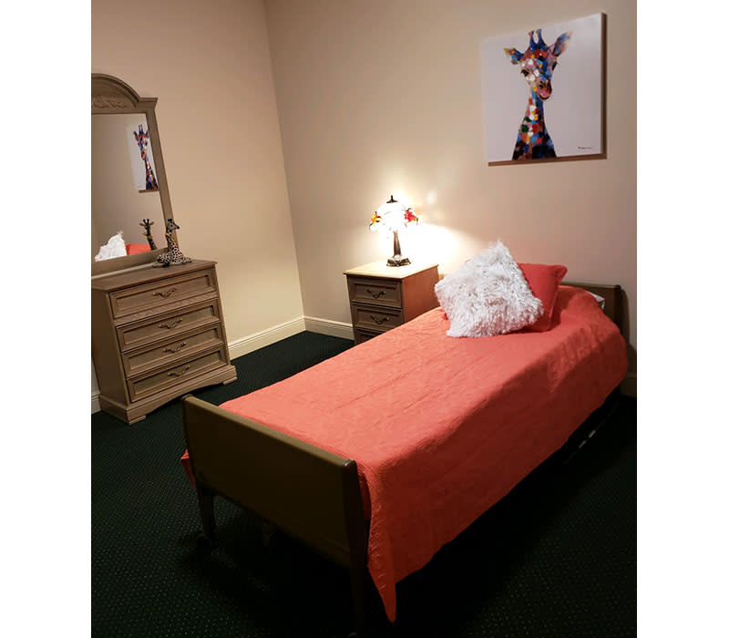 A cozy bedroom with a single bed and orange bedding, featuring a dresser and wall art.