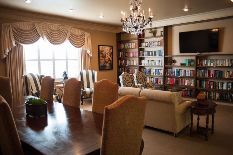 A cozy living room with bookshelves and a chandelier, featuring a dining area and comfortable seating.