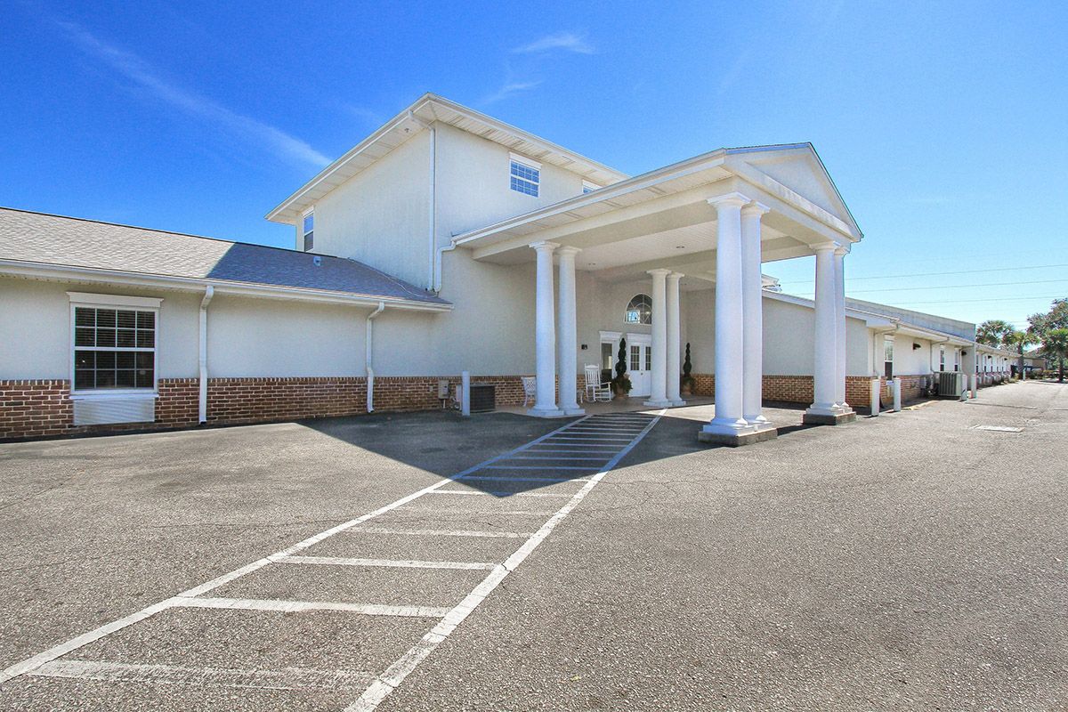 A white building with a columned entrance and adjacent parking area under a clear blue sky.