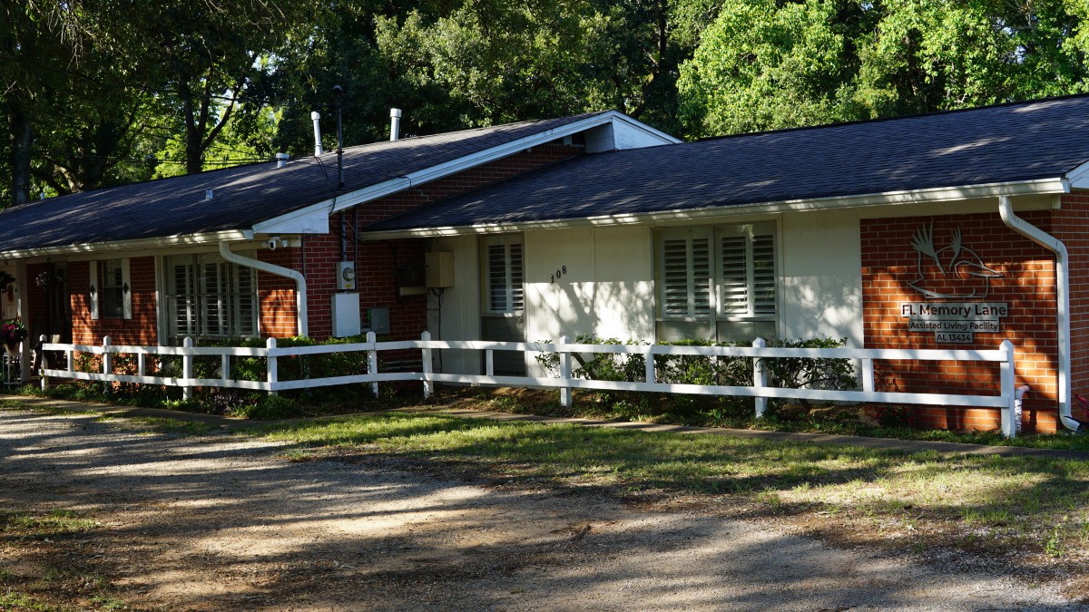 A suburban house with a white fence and surrounding trees.