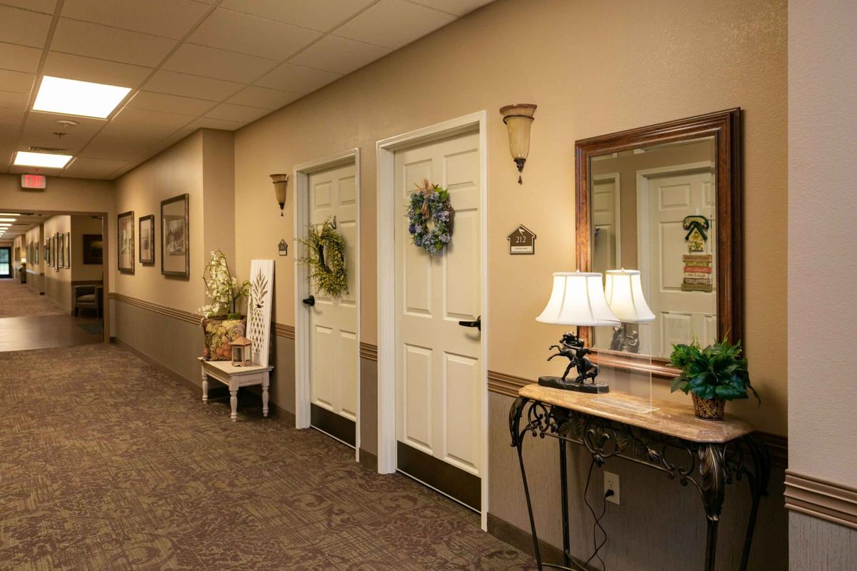 A warmly decorated hallway with doors adorned with wreaths, alongside a console table holding a lamp and mirror.