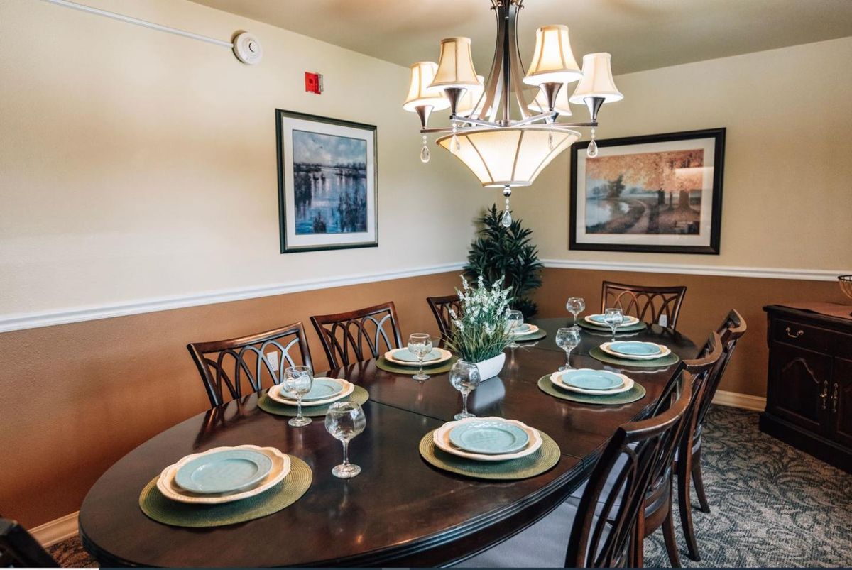 An elegantly set dining table with a chandelier and framed artwork in the background.