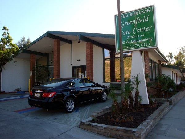 A clinic entrance with a car parked in the driveway and a sign displaying the name of the facility.