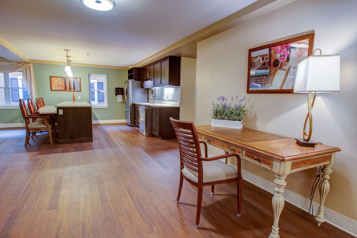 A modern kitchen and living space with wooden flooring, featuring a small desk and chair in the foreground.