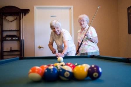 Two elderly women enjoying a game of billiards together.