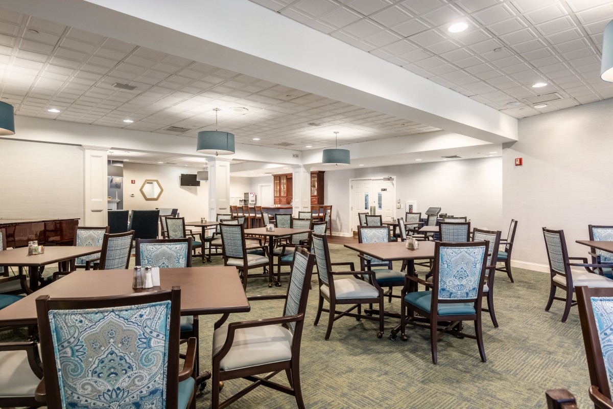 A spacious dining area with multiple tables and chairs arranged neatly under a well-lit ceiling.