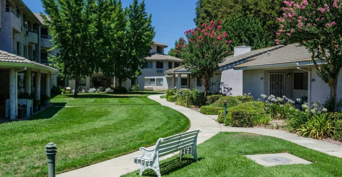 A serene residential area with a pathway and a bench surrounded by lush greenery.