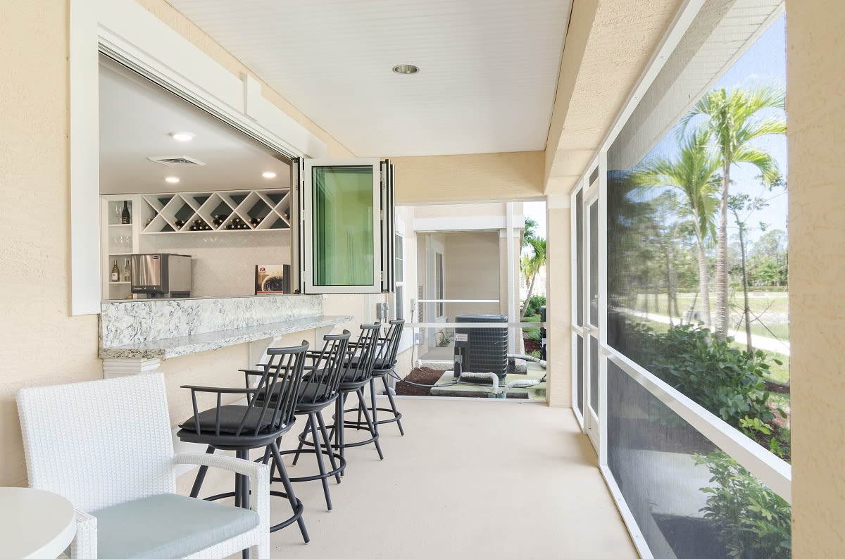 A spacious outdoor bar area with high chairs and a view of lush greenery.