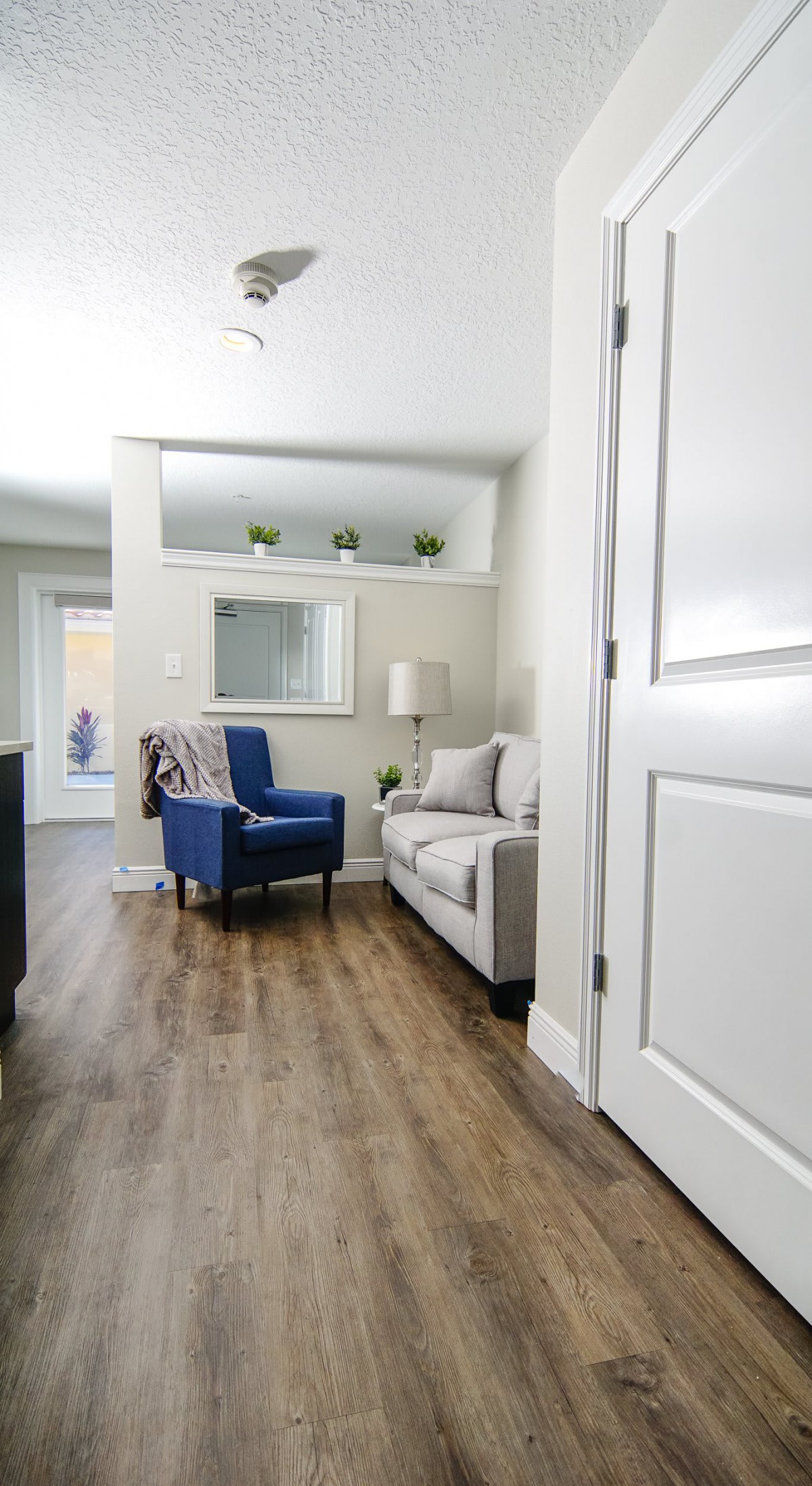A modern living room featuring a blue chair, cozy sofa, and wood flooring with neutral decor.