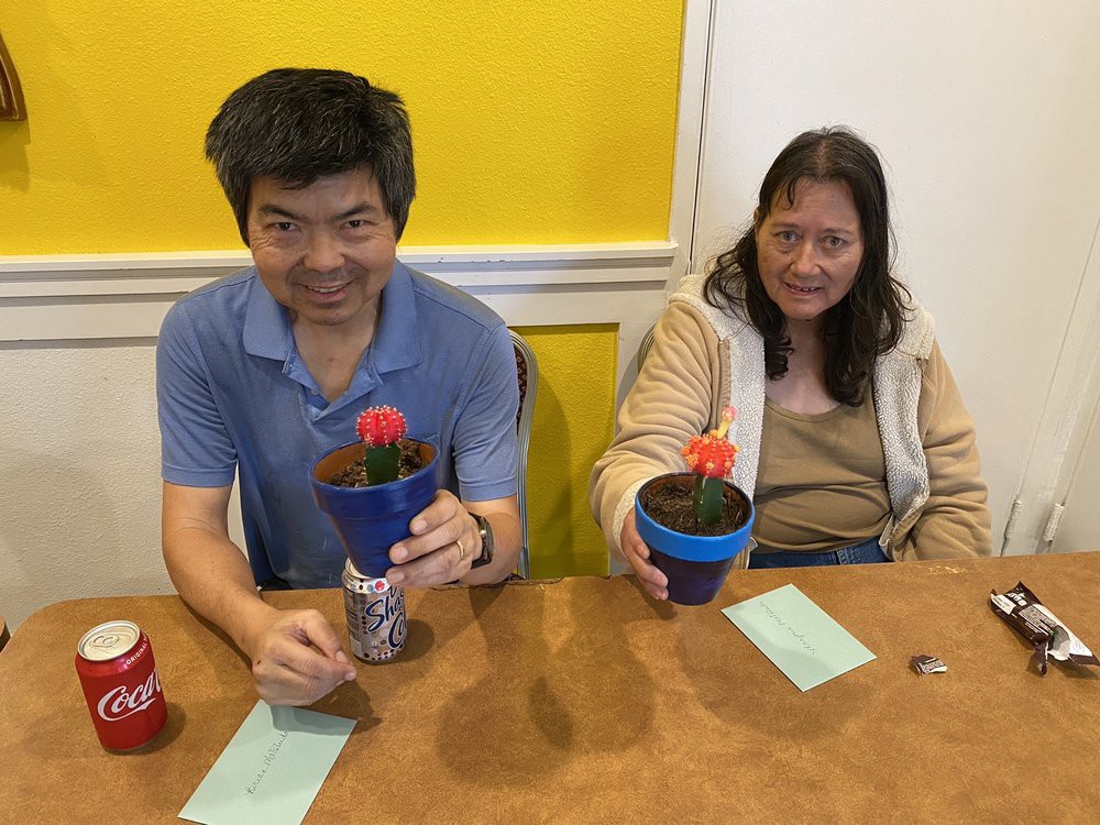 Two people sitting at a table, each holding a small potted cactus.