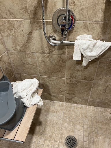 A corner of a bathroom shower area featuring towels and cleaning supplies.