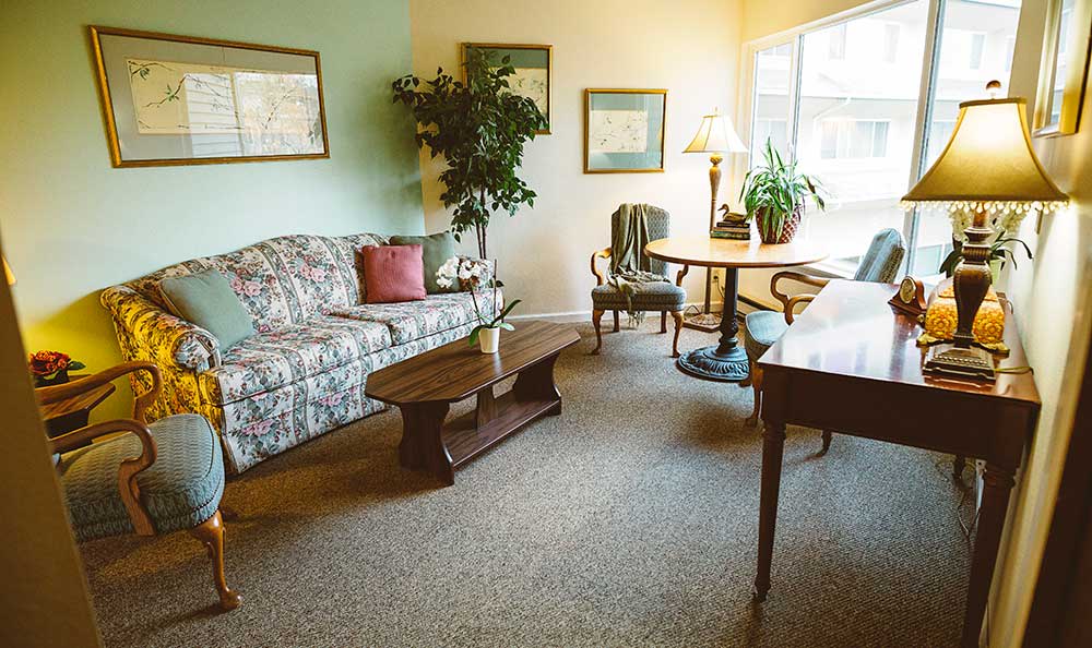 A cozy living room with a floral sofa, wooden coffee table, and indoor plants.