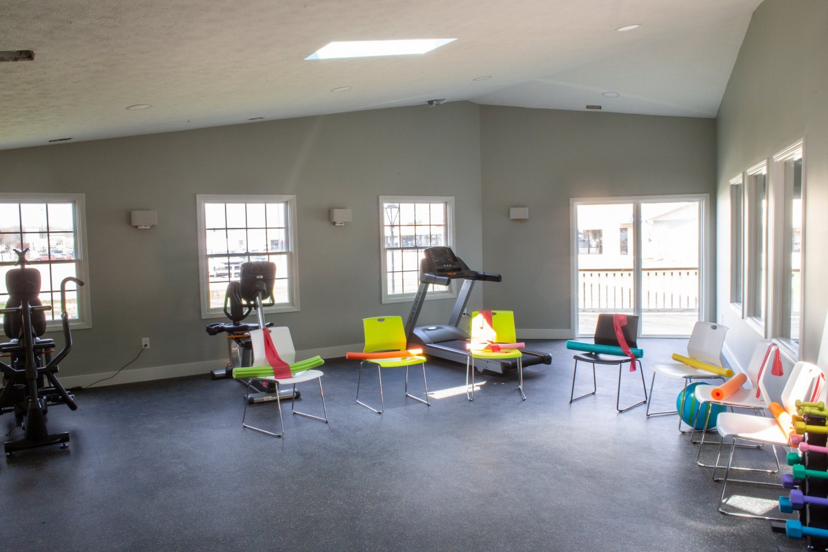 A small gym with exercise equipment and colorful chairs by the windows.