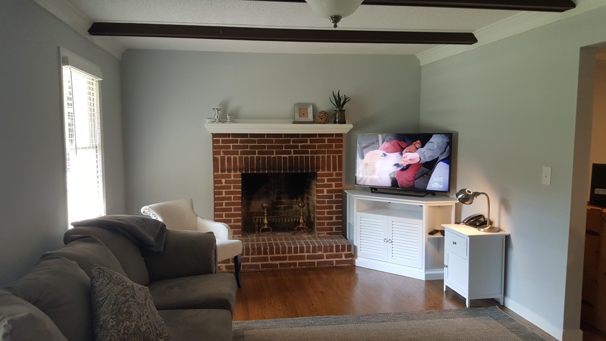 A cozy living room featuring a brick fireplace and a television next to a comfortable seating area.
