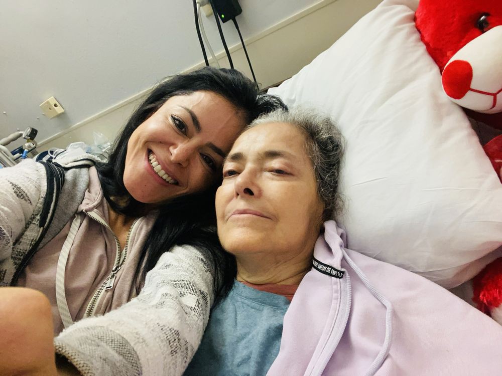 A woman takes a selfie with a patient in a hospital bed.