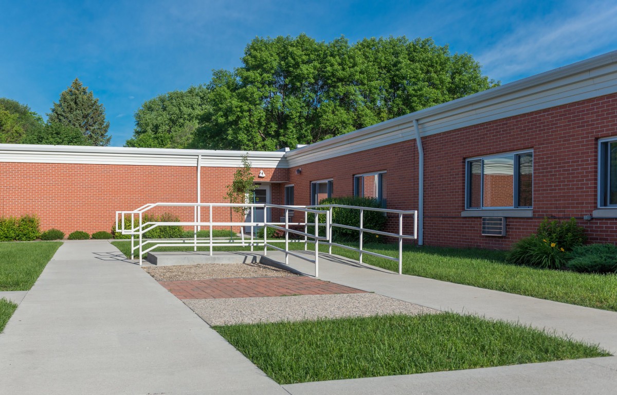A brick building with an accessibility ramp and surrounding greenery.