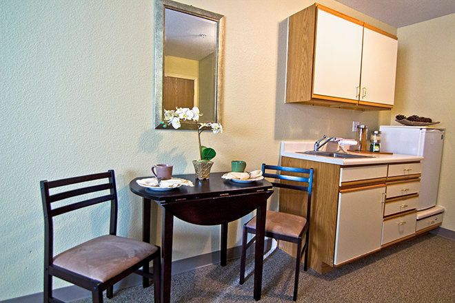 A compact kitchen and dining area with a small table and chairs, featuring a mirror and a simple setup.