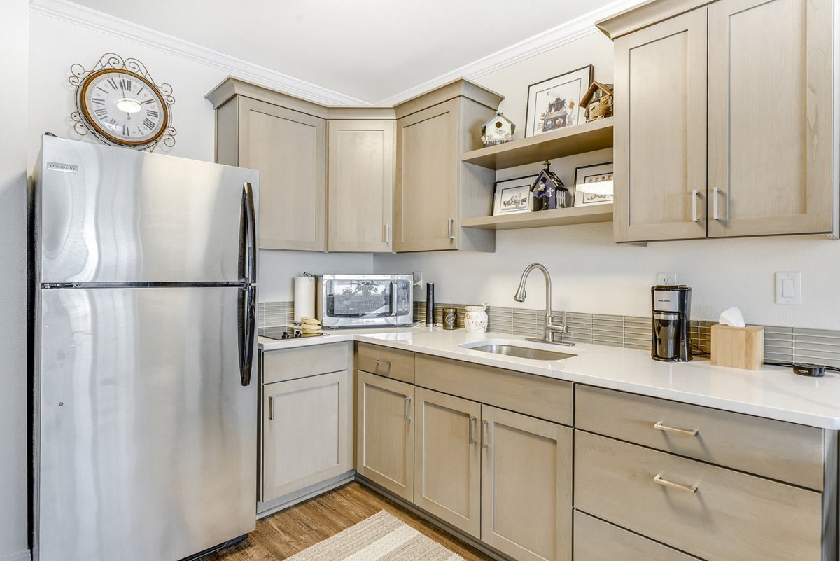 A modern kitchen featuring a stainless steel refrigerator, microwave, and beige cabinets with open shelving.