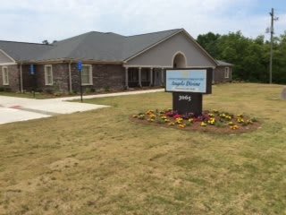 A church building with a sign in front, surrounded by grass and flowers.
