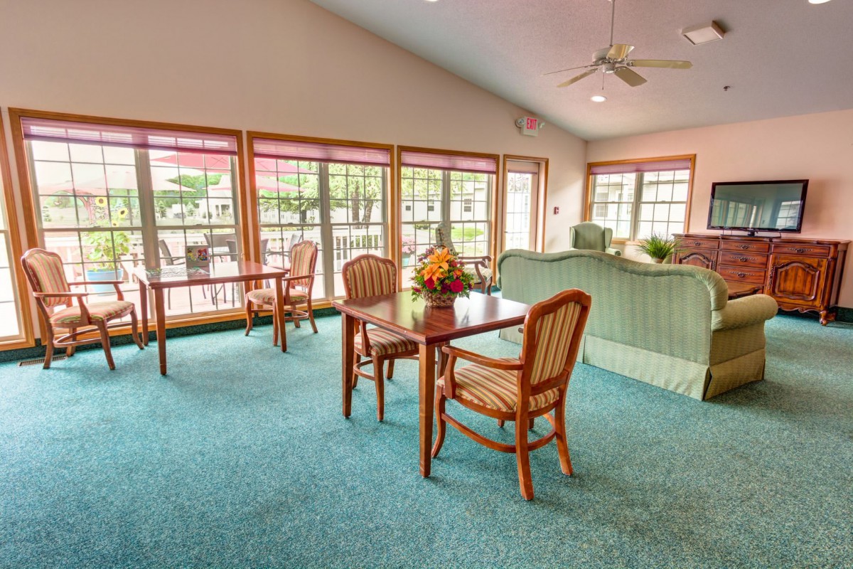 A cozy living room area with tables and chairs, featuring large windows that let in plenty of natural light.