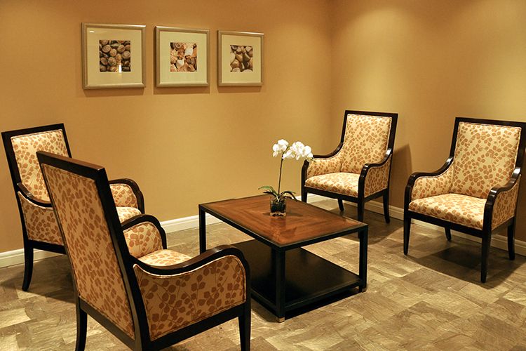 A cozy waiting room with elegant chairs and a table, adorned with artwork on the walls.