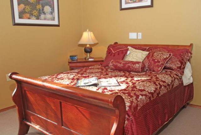 A cozy bedroom with a wooden bedframe, red and gold bedding, and a nightstand featuring a lamp.