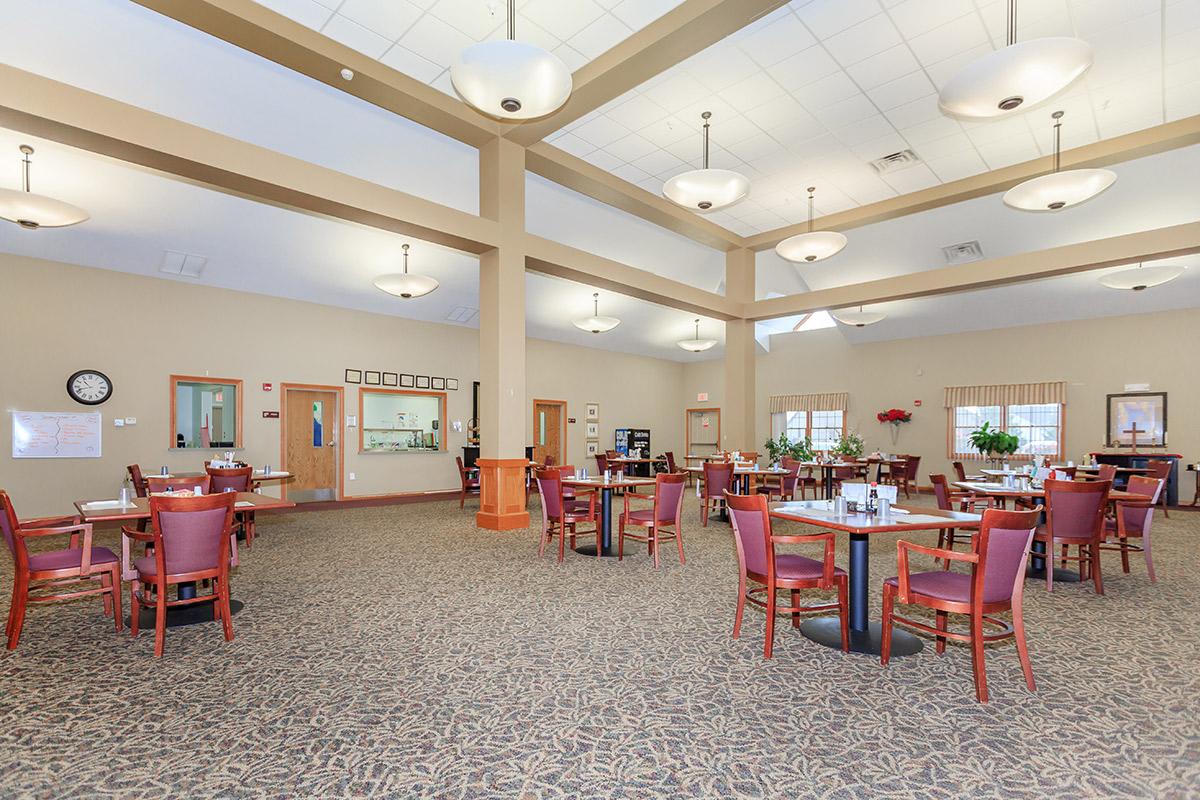 A spacious dining room with multiple tables and chairs, well-lit by ceiling lights.