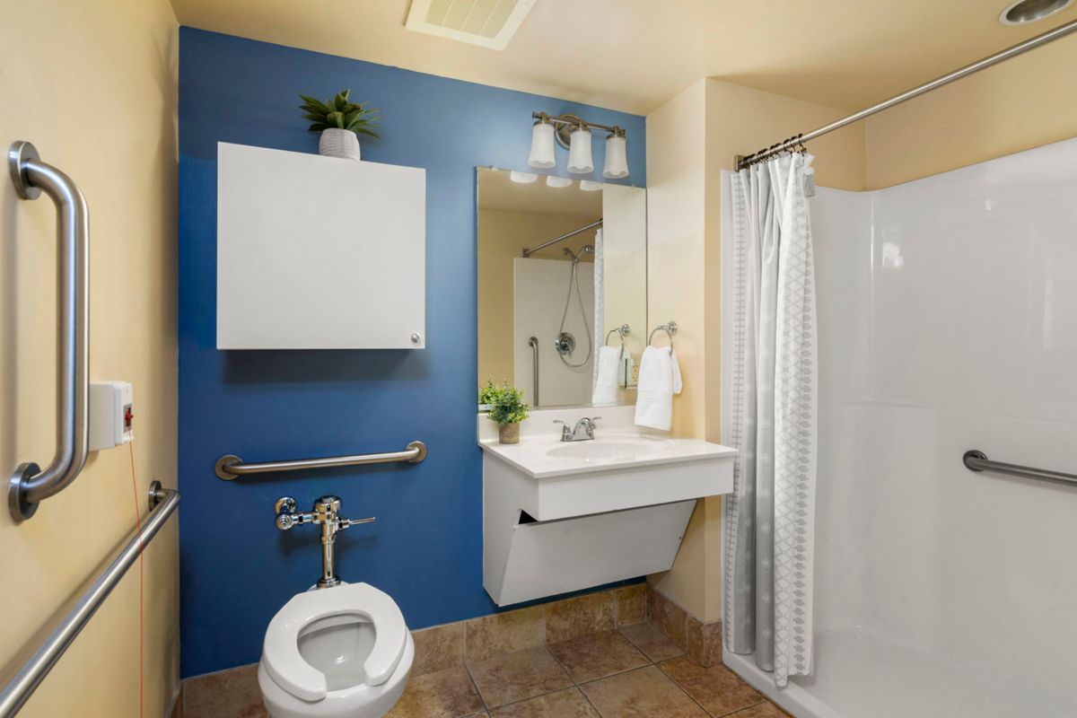 A modern bathroom with a blue accent wall, featuring a toilet, sink, mirror, and shower area.
