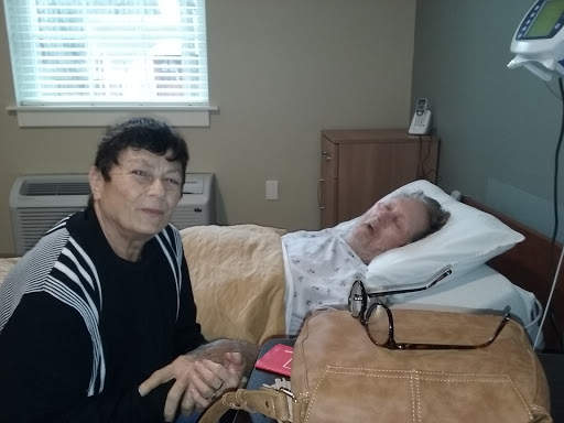 A caregiver sitting beside a patient in a hospital room, providing comfort and support.