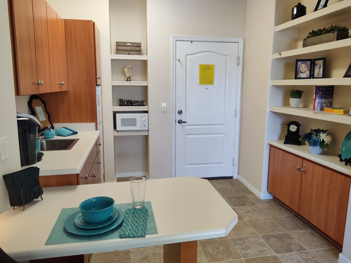 A modern kitchen with a dining area, featuring wooden cabinets, an open shelf concept, and teal-colored dishware.