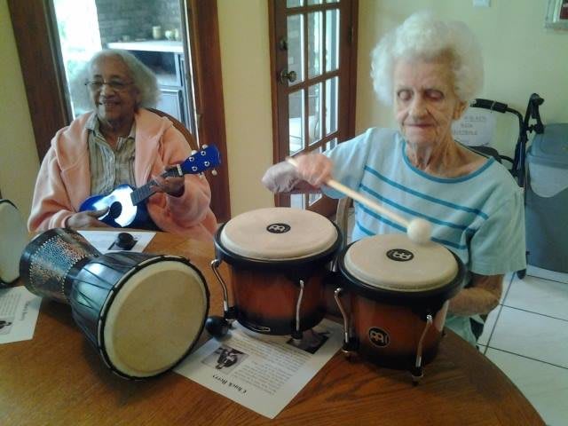 Two elderly women enjoying playing musical instruments together.