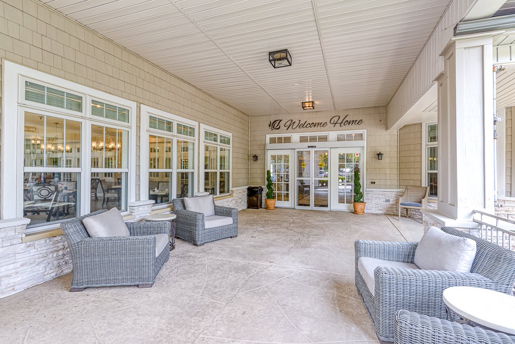 A spacious patio area with comfortable seating and large windows, leading to a building entrance.