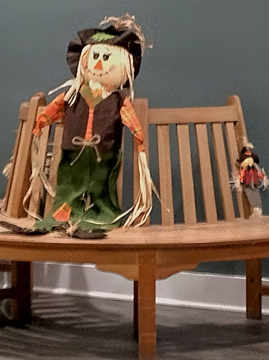 A handmade scarecrow sits on a wooden bench, adding a touch of autumn charm to the space.