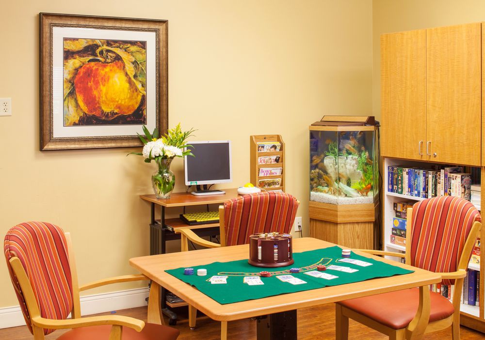 A cozy office space with a desk, computer, and artwork on the wall. There are chairs surrounding a table, an aquarium in the corner, and a bookshelf nearby.