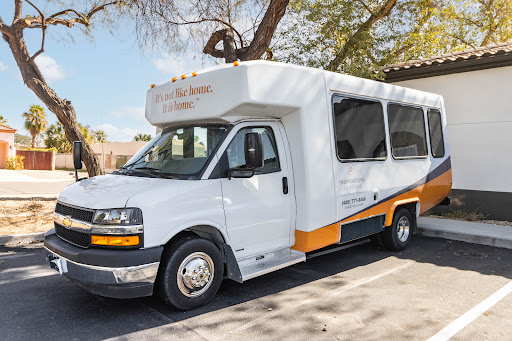 A white shuttle van parked under a tree, featuring an orange accent.