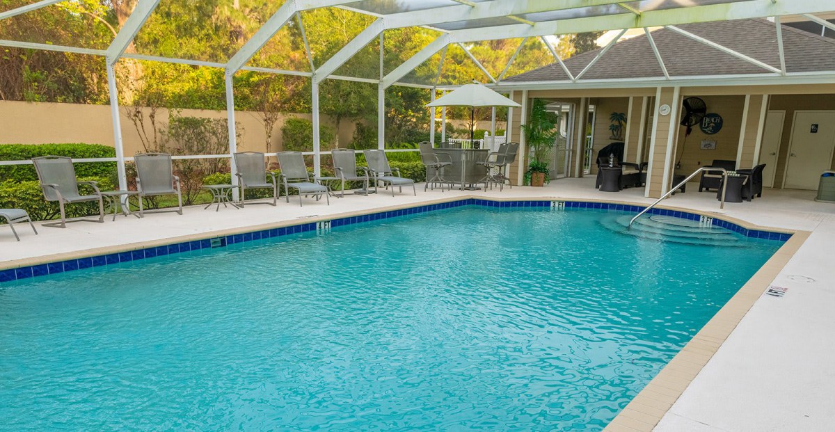 A serene outdoor swimming pool with a screen enclosure and patio seating.