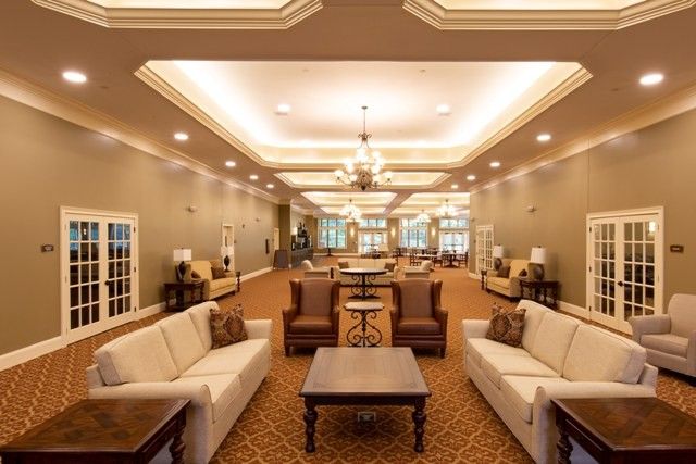 A spacious lobby area with elegant sofas, chairs, and tables arranged on a carpeted floor, illuminated by ceiling lights.