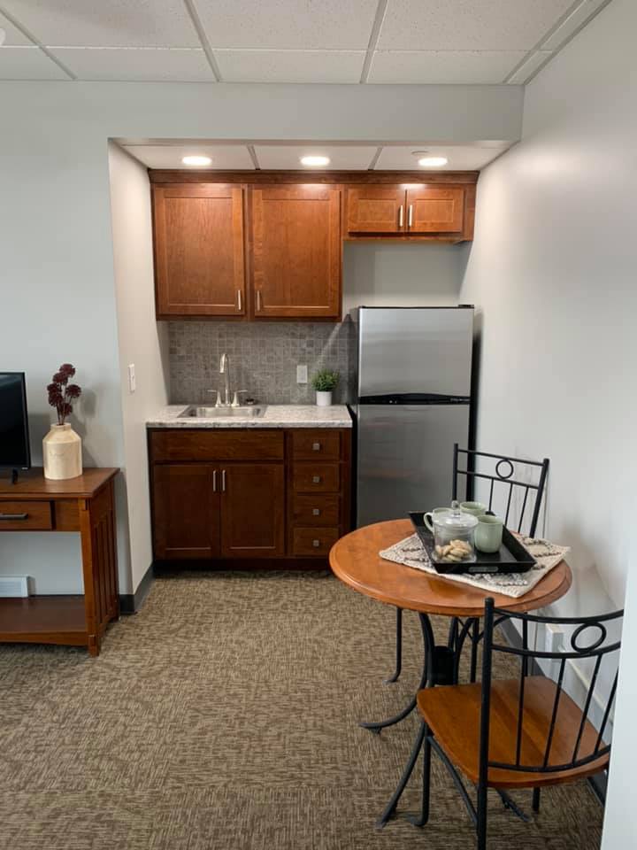 A compact kitchenette with wooden cabinets, a small fridge, and a cozy dining setup featuring a round table with chairs.