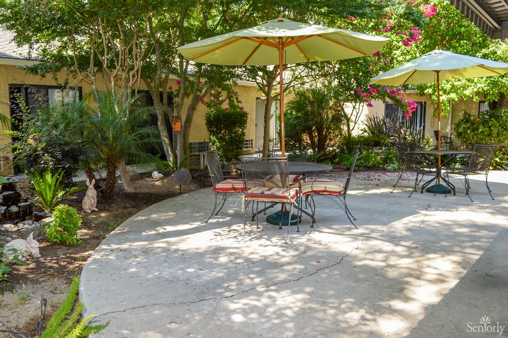 A tranquil patio setting with chairs and tables under large umbrellas, surrounded by greenery.